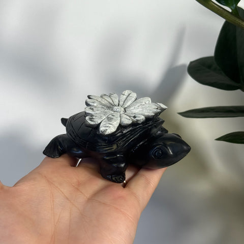 Black chrysanthemum stone turtle figurine with a white floral carving on its shell.