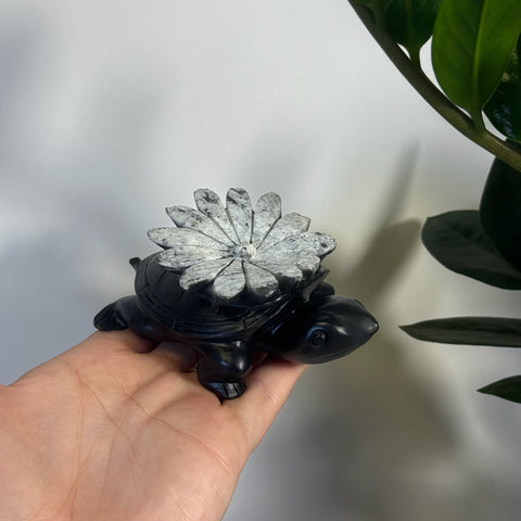 Black chrysanthemum stone turtle figurine with a white floral shell, held in a hand.