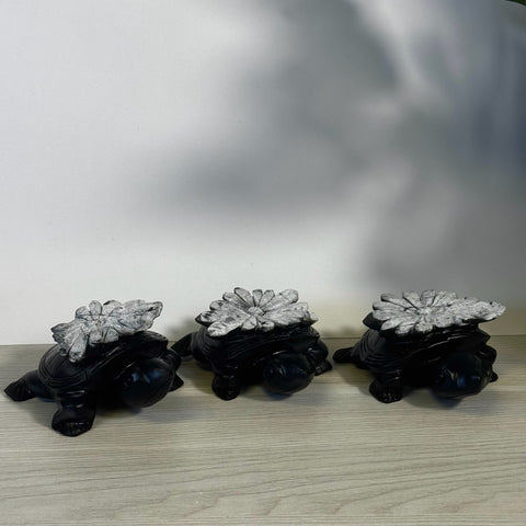 Three black stone turtles with textured gray chrysanthemum stone shells on a light wood surface.