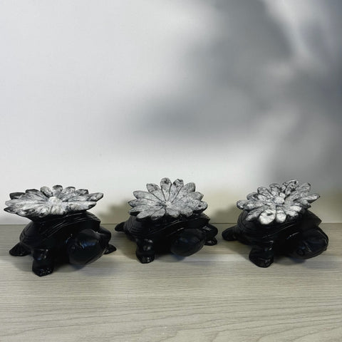 Three black stone turtles with white chrysanthemum stone shells on a wooden surface.