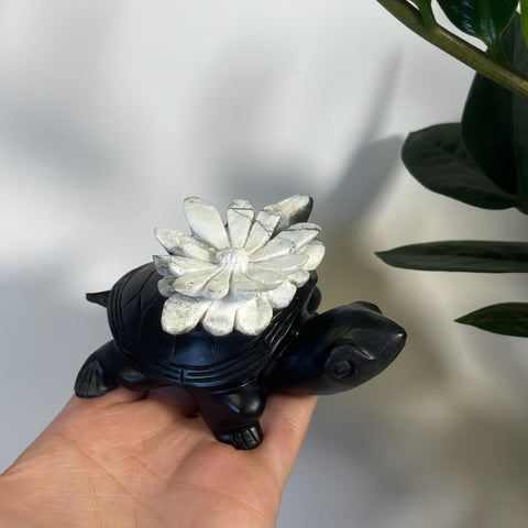 Black Chrysanthemum Stone Turtle with a white carved flower on its shell, held in a hand.