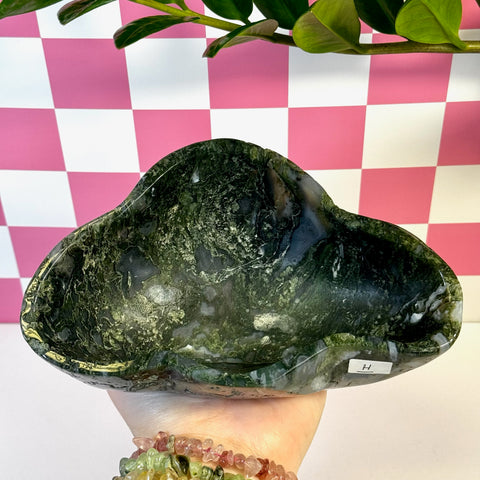Curvy moss agate bowl, dark green with white swirls, held in hand against a pink and white checkered background.