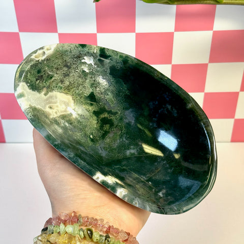 Curvy moss agate bowl with deep green, white, and clear patterns, held against a pink and white checkered background.