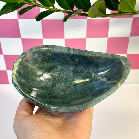 Curvy moss agate bowl, deep green with white inclusions, held in hand against a pink and white checkered background.