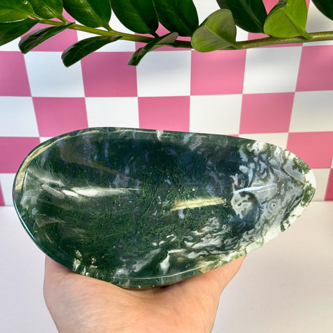 Curvy moss agate bowl, deep green with white inclusions, held against a pink and white checkered background.