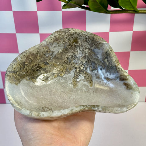Hand holding a polished, curvy moss agate bowl with natural white, brown, and gray patterns.