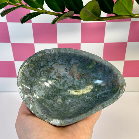 Curvy moss agate bowl, deep green with white and reddish-brown inclusions, held in a hand.