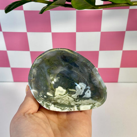 Curvy moss agate bowl with deep green, white, and clear patterns, held against a pink and white checkered background.