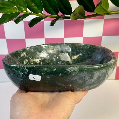 Curvy moss agate bowl, deep green with white inclusions, held in hand against pink and white checkered background.