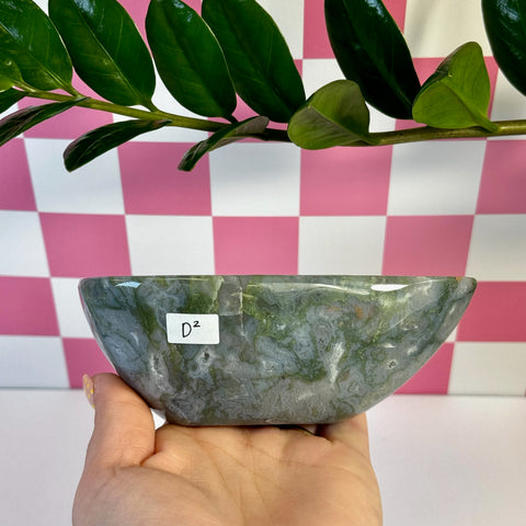 Curvy moss agate bowl, green and white swirled, held in hand against a pink checkered background.
