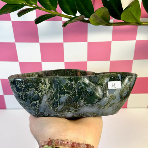 Curvy moss agate bowl, dark green with white veins, held against a pink checkered background.