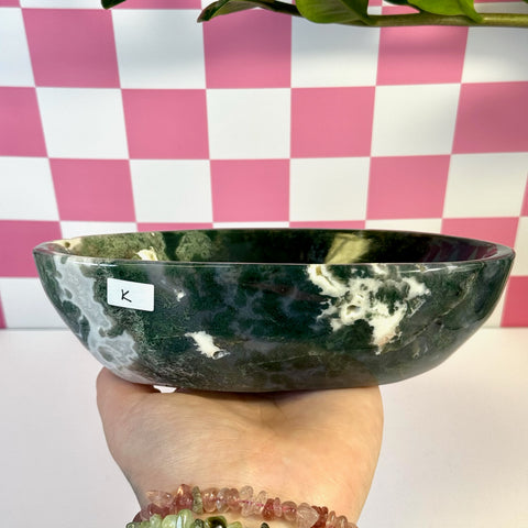 Curvy moss agate bowl, dark green with white inclusions, held in hand against pink checkered background.