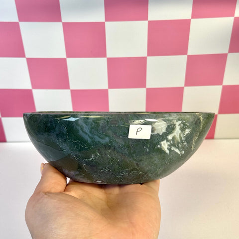 Curvy moss agate bowl, dark green with white inclusions, held in hand against a pink and white checkered background.