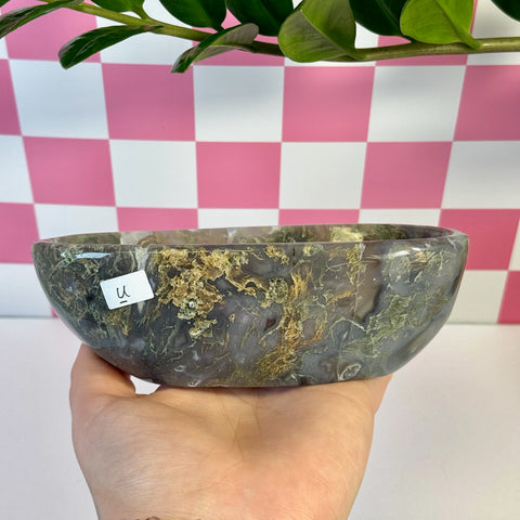 Curvy moss agate bowl, natural green and brown patterns, held in hand against pink checkered background.