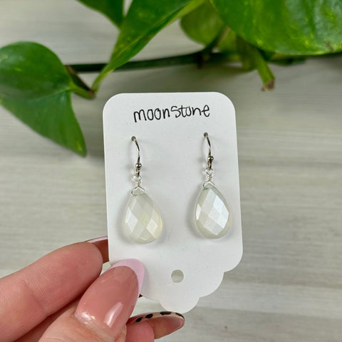 Faceted teardrop moonstone earrings with silver hooks on a white display card.