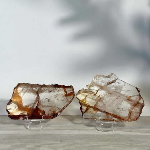 Two raw, clear Fire Quartz slices with reddish-brown inclusions on clear stands.