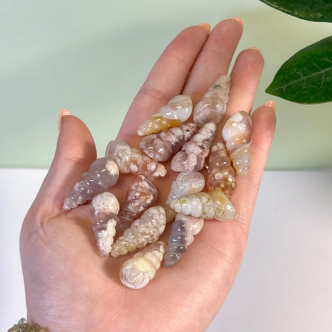 Hand holding multiple small, polished flower agate spiral shells in varying natural pink, cream, and brown tones.