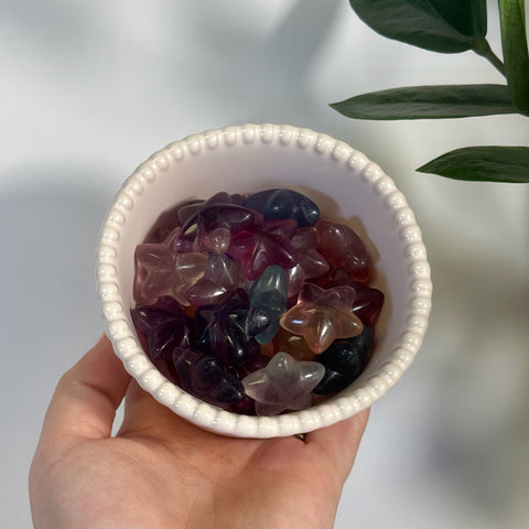 Small white bowl filled with polished fluorite sea star carvings in purple, pink, and clear hues.