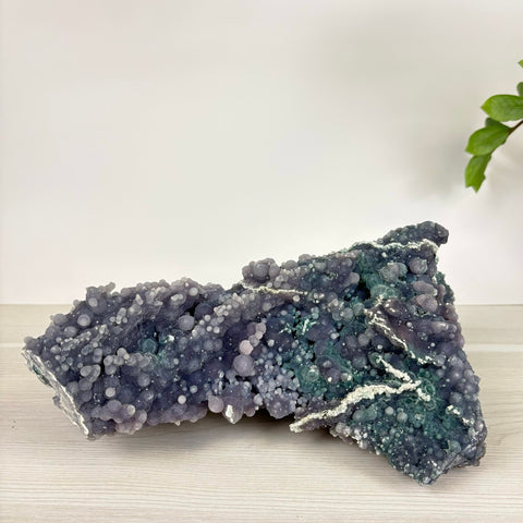Large grape agate specimen featuring deep purple and teal botryoidal crystal clusters on a white wooden surface.