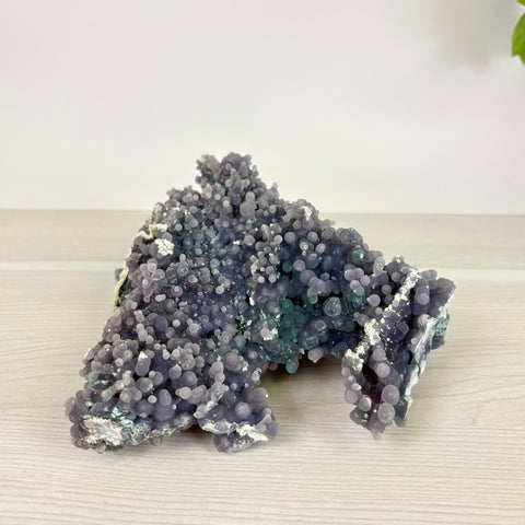 Deep purple grape agate cluster with botryoidal, sphere-like formations on a light wood surface.