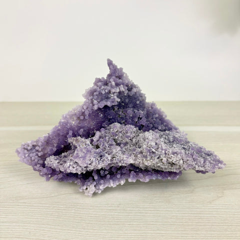 Pyramidal grape agate cluster with deep purple, spherical botryoidal crystals on a light wooden surface.