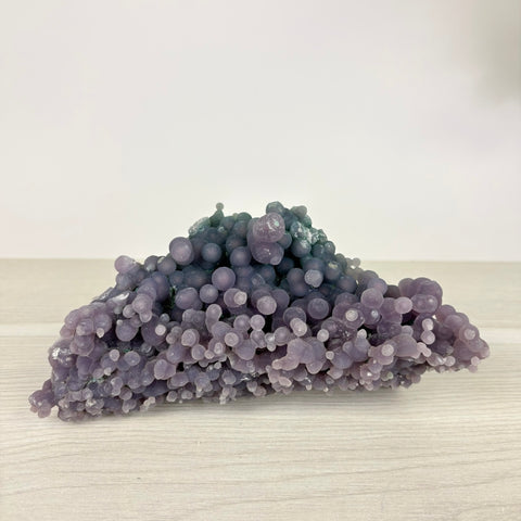 Grape agate specimen featuring clusters of translucent, spherical purple crystals on a light wooden surface.