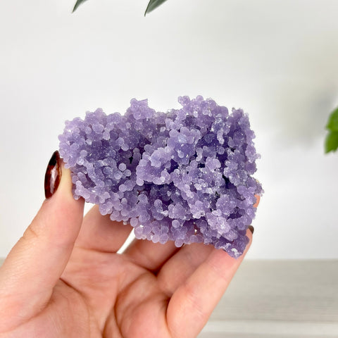 Hand holding a cluster of vibrant purple grape agate with small, bubbly, crystalline formations.