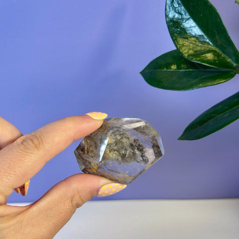 Hand holding a faceted Garden Quartz free form with clear and earthy inclusions.