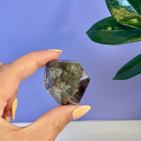Hand holding a faceted garden quartz free form with green and brown inclusions.