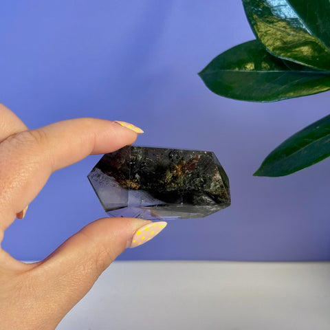 Hand holding a dark Garden Quartz free form with visible mineral inclusions.