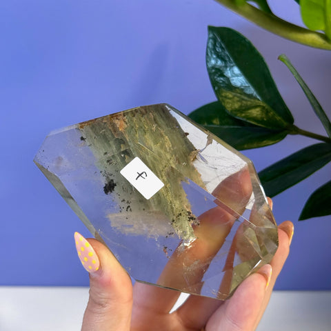 Clear garden quartz free form with green inclusions held by a hand with yellow polka dot nails.