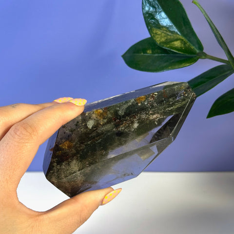Hand holding a dark green and clear Garden Quartz free form with natural inclusions.