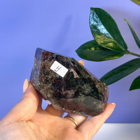 Dark garden quartz free form crystal with natural inclusions, held in a hand.