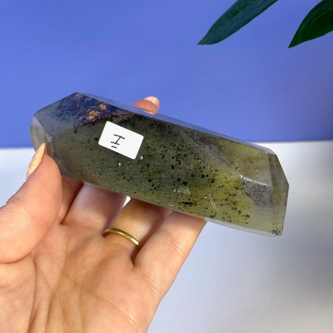 Hand holding a faceted Garden Quartz Free Form, showcasing its green hues and dark inclusions.