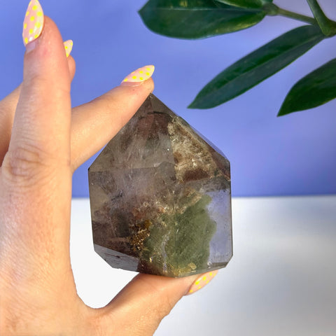 Garden Quartz Free Form, a clear crystal with green and brown inclusions, held by a hand.