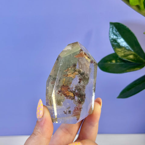 Clear Garden Quartz free form with green, red, and black mineral inclusions, held by a hand.