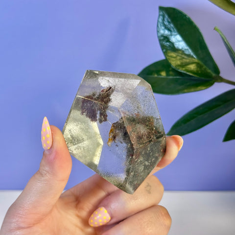 Clear garden quartz free form with dark green and reddish mineral inclusions.