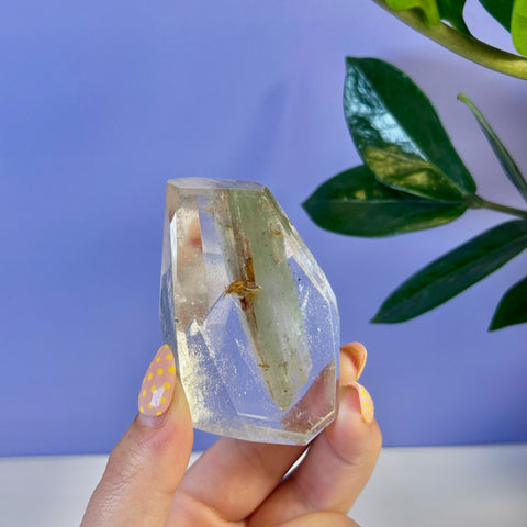 Clear garden quartz free form with green and brown inclusions, held by a hand with yellow polka dot nails.