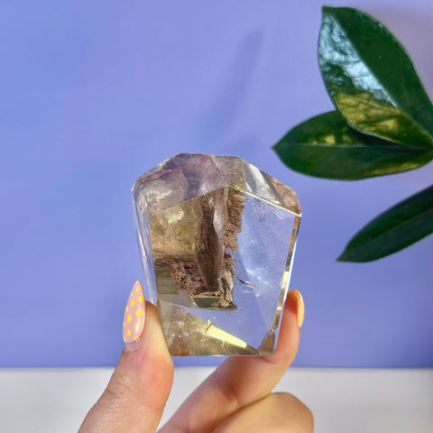 Clear garden quartz free form crystal with earthy inclusions, held by fingers with yellow polka dot nails.