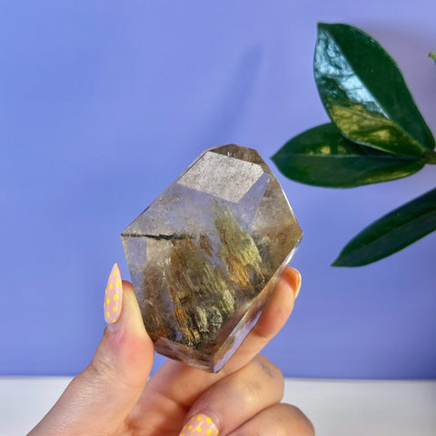 Garden Quartz free form crystal with earthy green and brown inclusions, held by a hand with yellow polka dot nails.