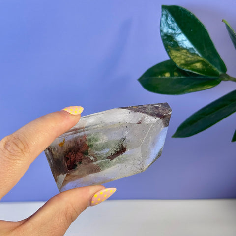 Clear garden quartz free form with red and green inclusions, held by a hand.