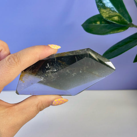 Garden Quartz free form, clear with dark inclusions, held by a hand with yellow polka dot nails.