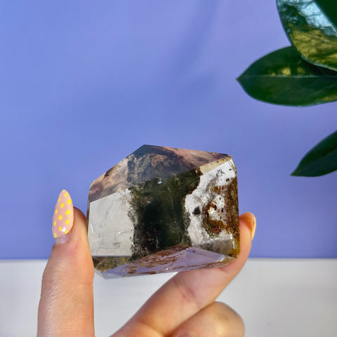 Garden Quartz free form with clear, green, and reddish-brown inclusions, held by fingers with yellow polka dot nails.