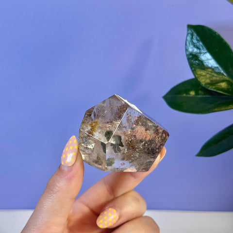 Garden Quartz Free Form held by hand, showcasing clear crystal with green and reddish mineral inclusions.