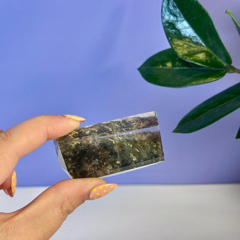Hand holding a translucent Garden Quartz free form with dark green and brown inclusions.