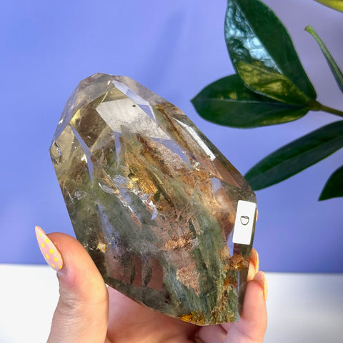 Faceted garden quartz free form with green and brown mineral inclusions, held in a hand.