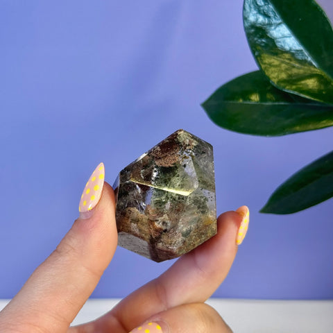 Hand holding a faceted Garden Quartz Free Form with green and brown inclusions.