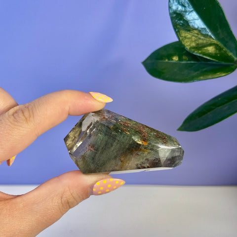 Hand holding a faceted Garden Quartz free form with green, brown, and red inclusions.