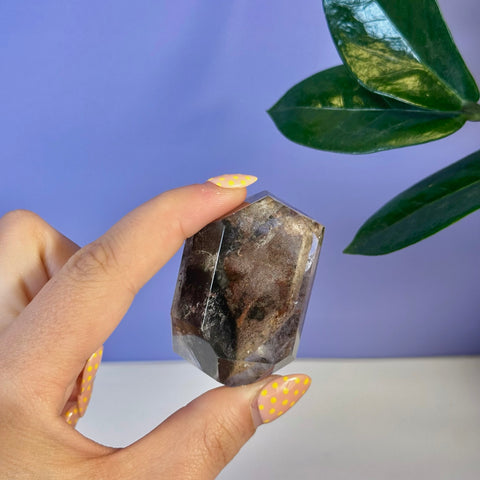 Hand holding a dark brown Garden Quartz free form crystal with natural inclusions.