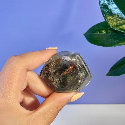 Hand holding a faceted Garden Quartz free form with dark green, red, and brown inclusions.